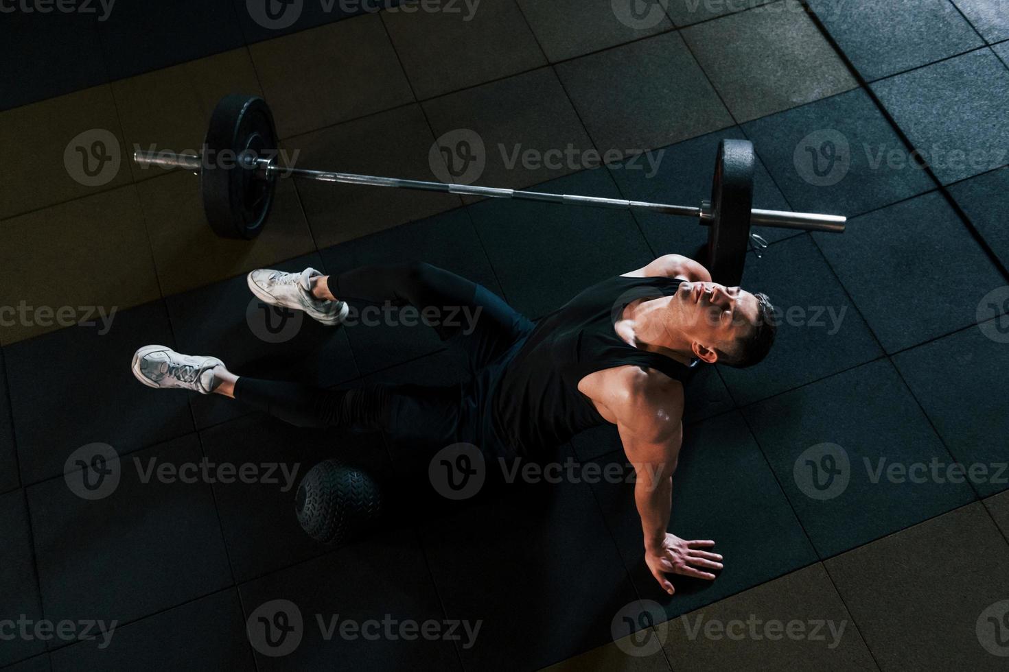 Top view of strong man in sportive clothes that sitting on the floor and takes a break in the gym photo