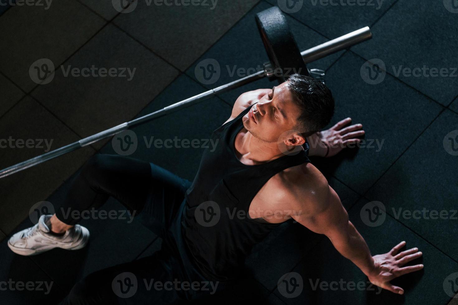 vista superior de un hombre fuerte con ropa deportiva que se sienta en el suelo y toma un descanso en el gimnasio foto