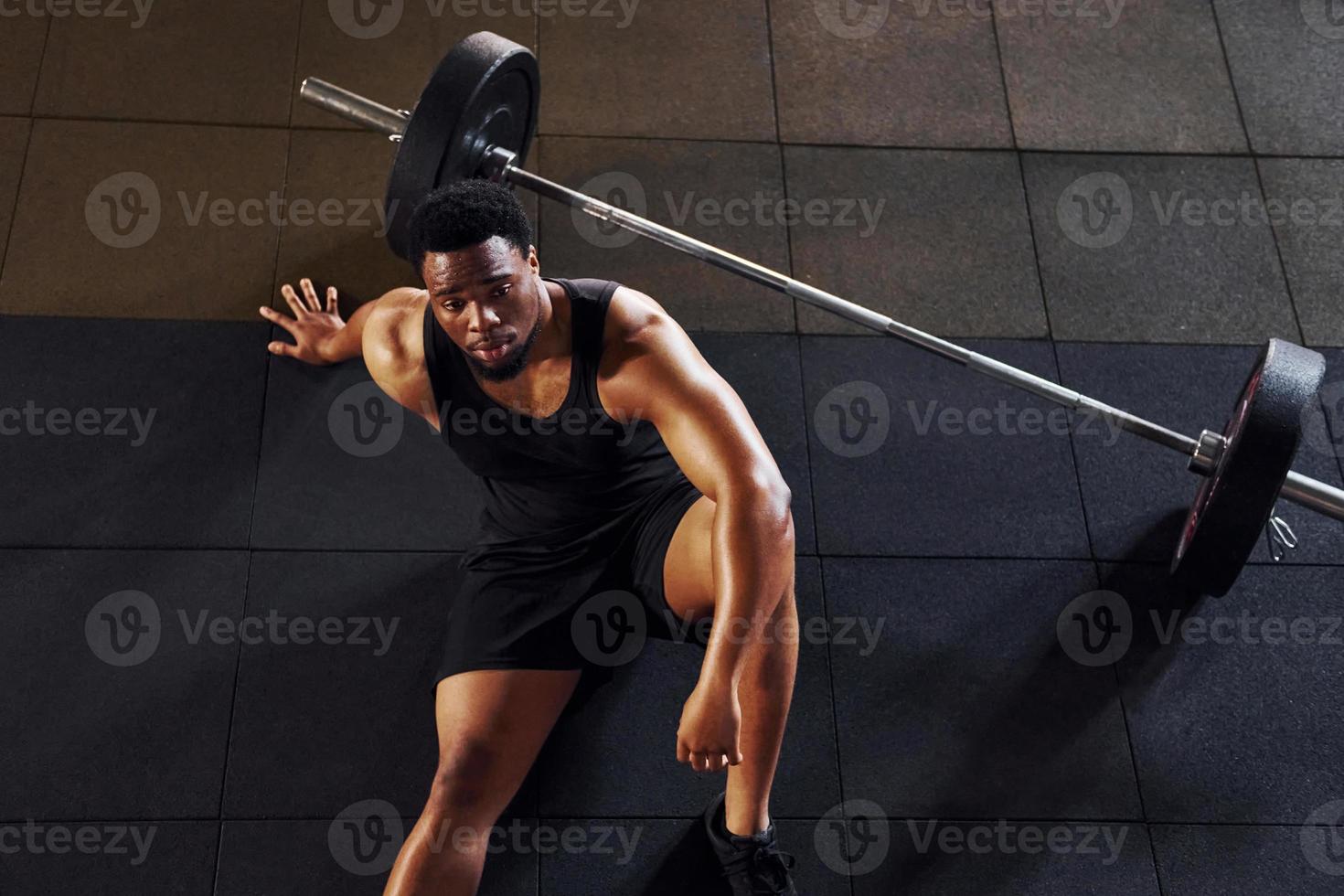 Sitting on the floor. Strong african american man in sportive clothes have workout day in the gym photo