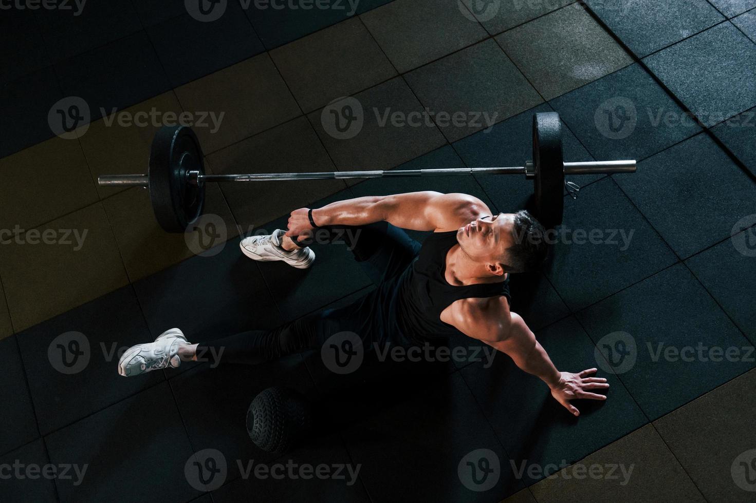 Top view of strong man in sportive clothes that sitting on the floor and takes a break in the gym photo