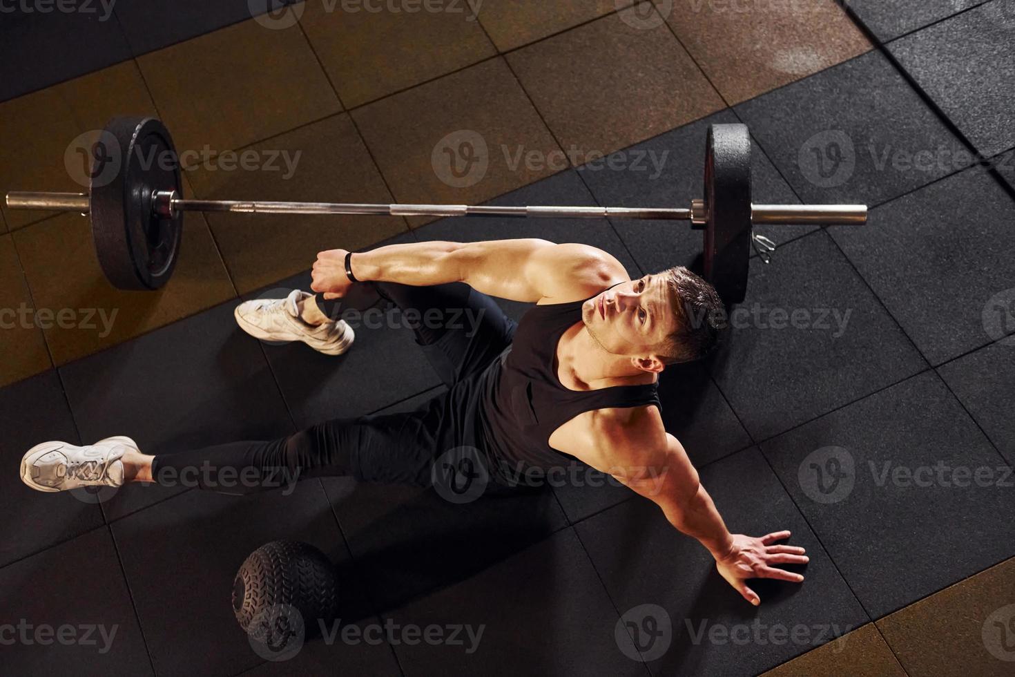 Top view of strong man in sportive clothes that sitting on the floor and takes a break in the gym photo