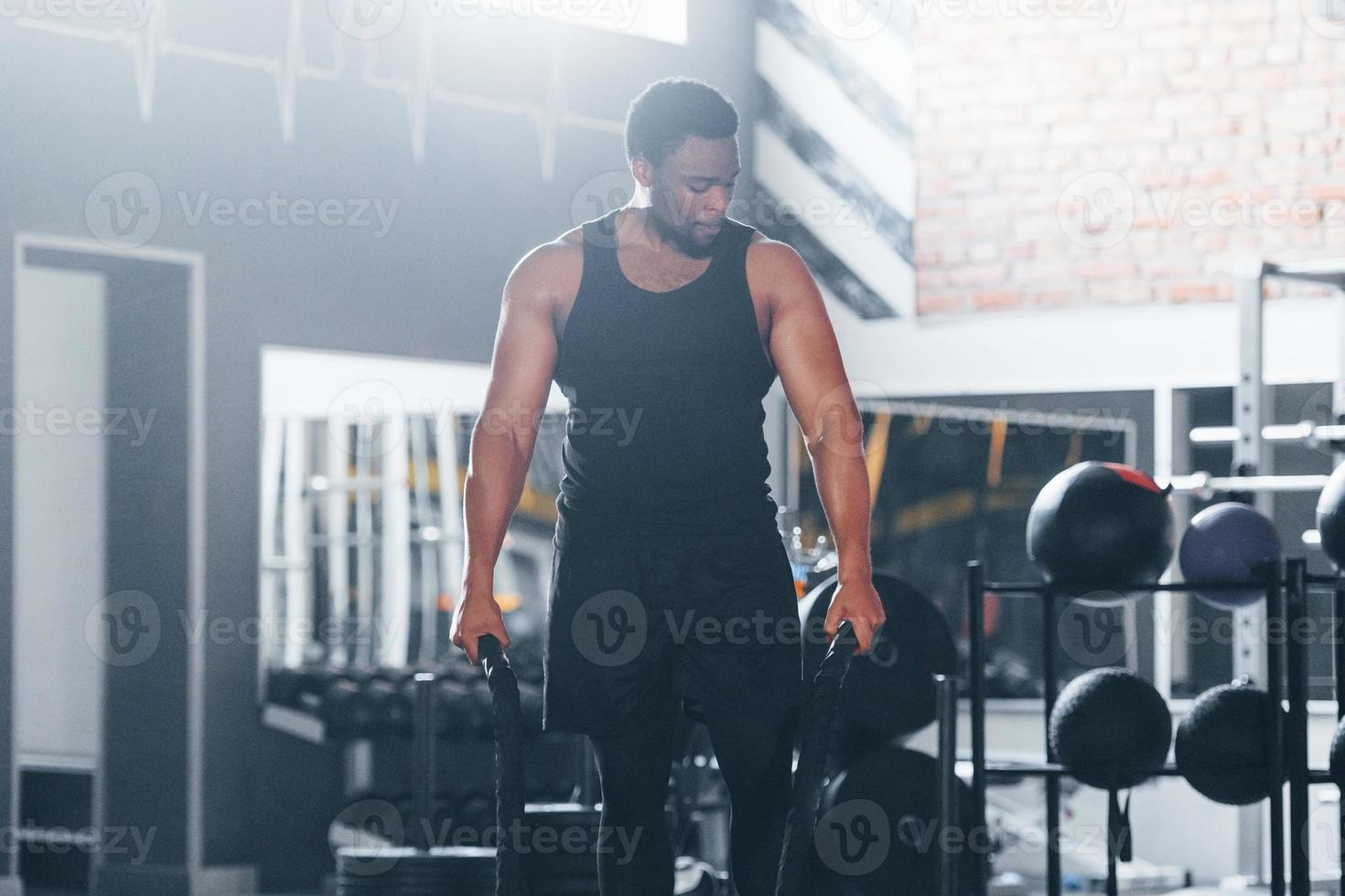 un hombre afroamericano fuerte con ropa deportiva tiene un día de  entrenamiento en el gimnasio. haciendo crossfit usando cuerdas 15293887  Foto de stock en Vecteezy