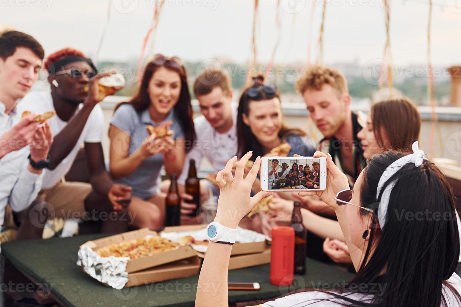 With delicious pizza. Group of young people in casual clothes have a party at rooftop together at daytime photo