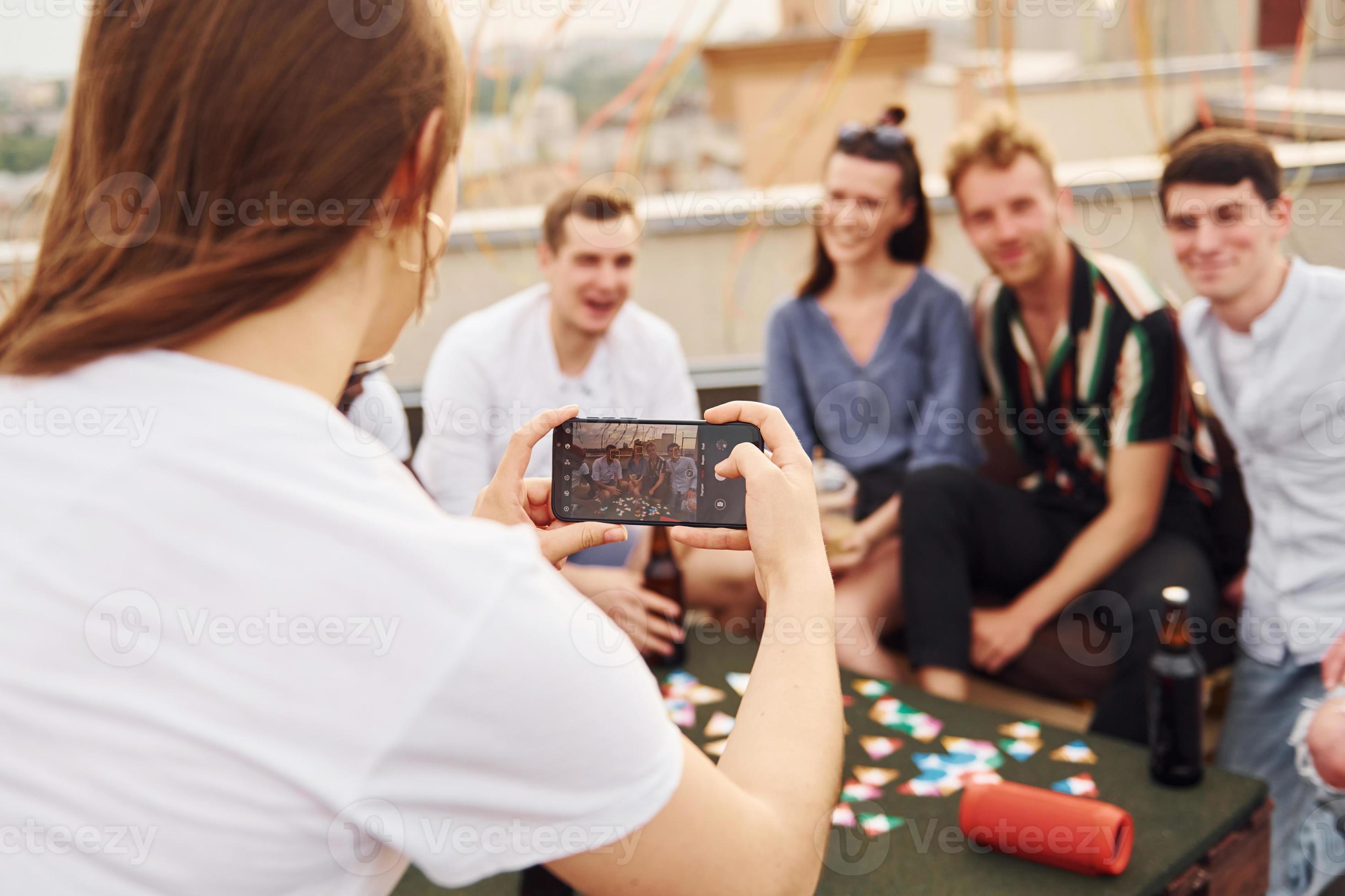 Girl doing photo when people playing card game. Group of young people