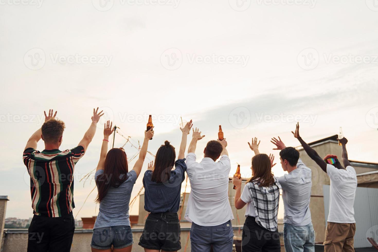 de pie alto y mirando el cielo nublado. un grupo de jóvenes con ropa informal tienen una fiesta en la azotea juntos durante el día foto