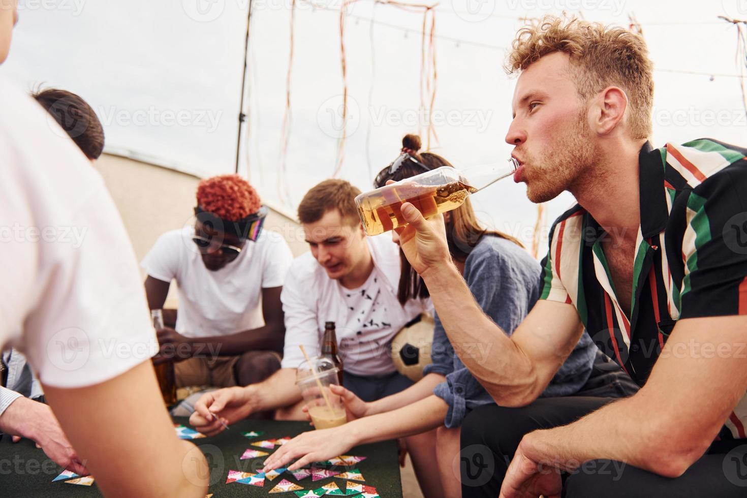 Playing card game. Group of young people in casual clothes have a party at rooftop together at daytime photo
