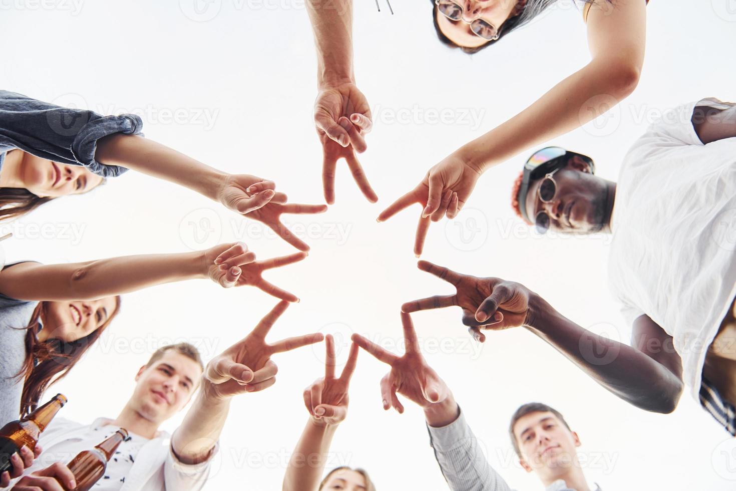 Making beautiful gesture by fingers. View from below. Group of young people in casual clothes have a party at rooftop together at daytime photo