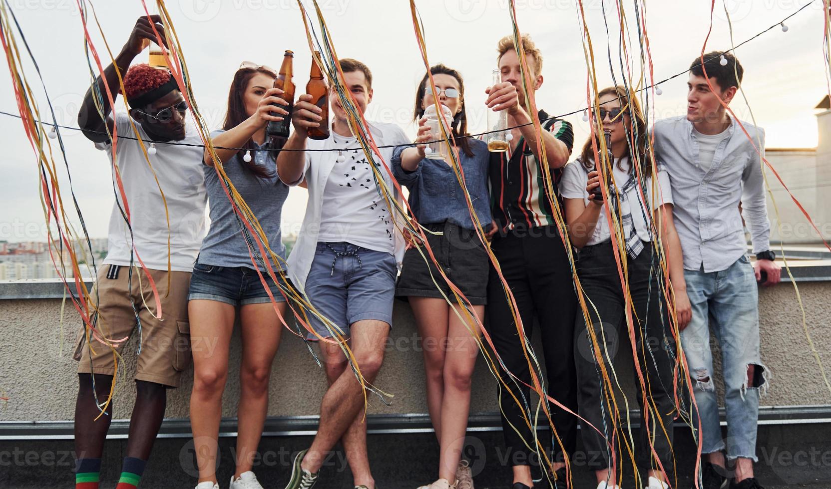 Leaning on the edge of the rooftop with decorates. Group of young people in casual clothes have a party together at daytime photo