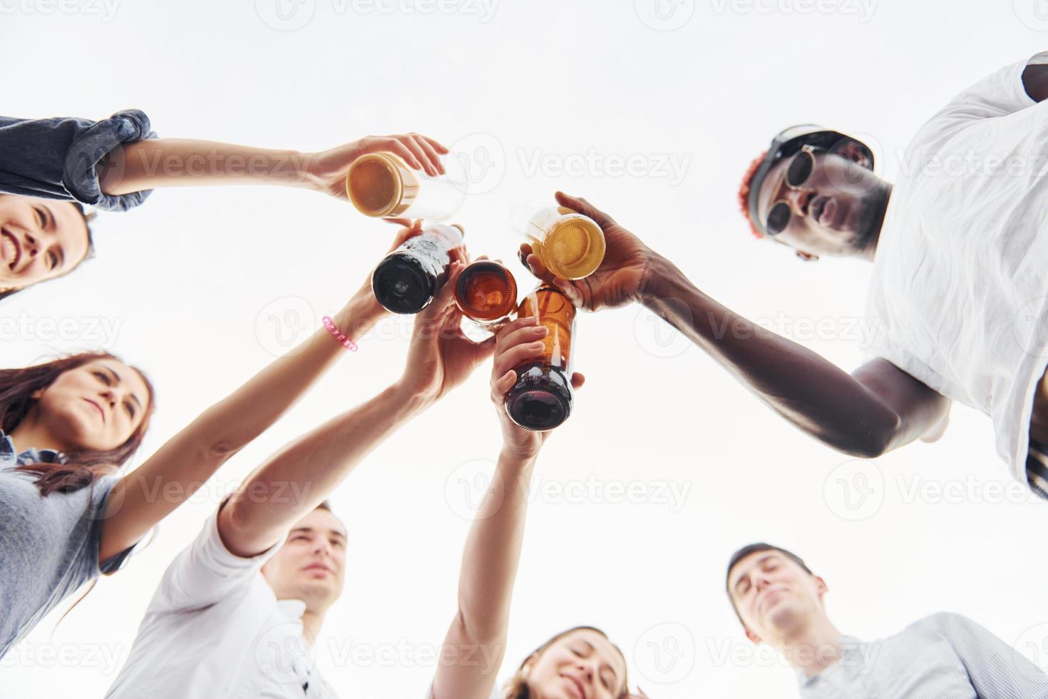 View from below. Doing cheers. Group of young people in casual clothes have a party at rooftop together at daytime photo