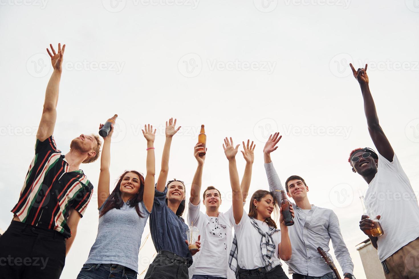 de pie alto y mirando el cielo nublado. un grupo de jóvenes con ropa informal tienen una fiesta en la azotea juntos durante el día foto