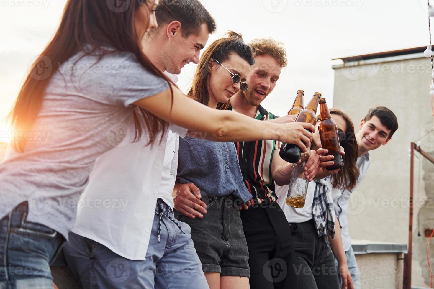 apoyándose en el borde de la azotea con decoraciones. grupo de jóvenes con ropa informal tienen una fiesta juntos durante el día foto