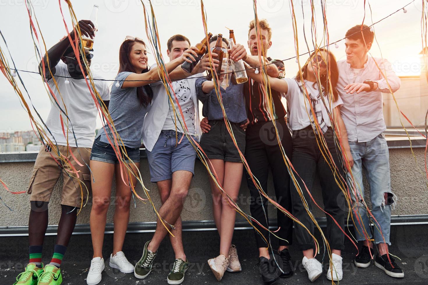 Leaning on the edge of the rooftop with decorates. Group of young people in casual clothes have a party together at daytime photo