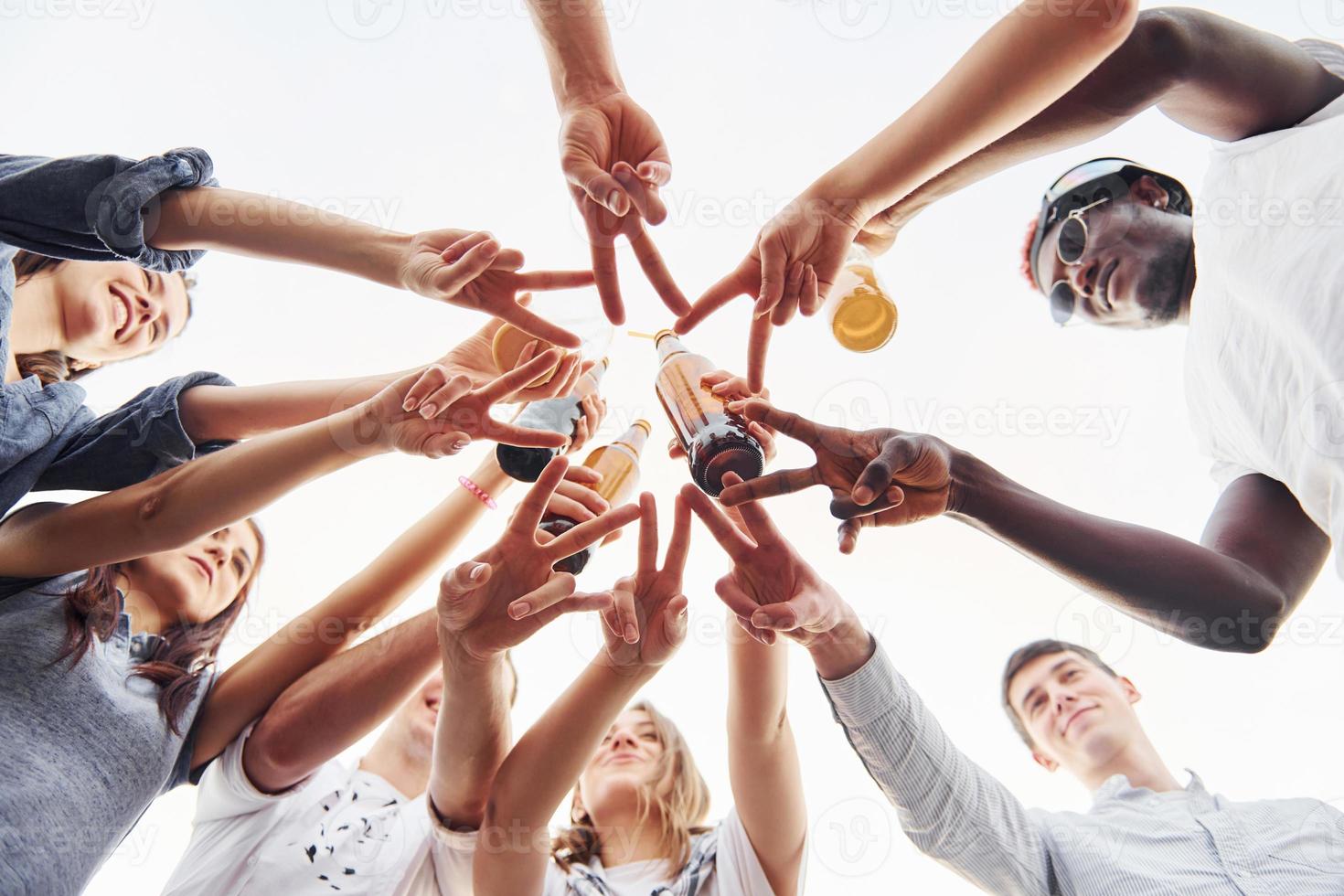 Making beautiful gesture by fingers. View from below. Group of young people in casual clothes have a party at rooftop together at daytime photo