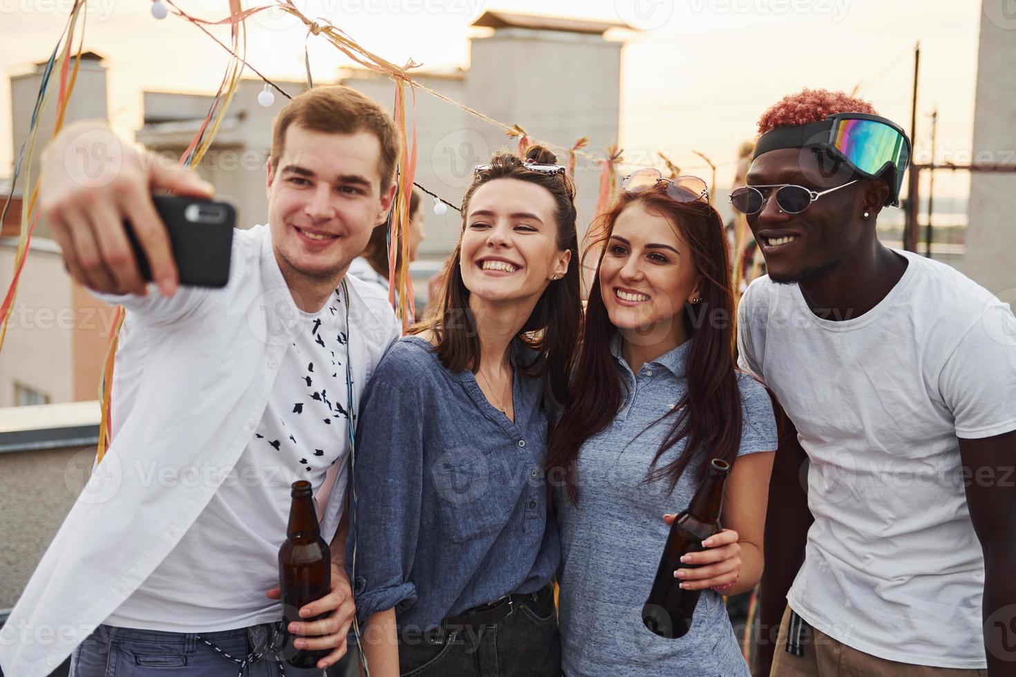 Group of young people in casual clothes have a party at rooftop together at daytime and doing selfie by phone photo