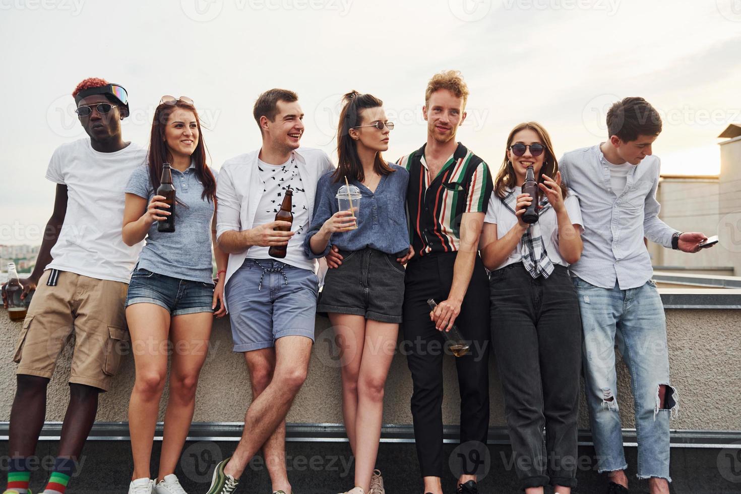 Standing with alcohol at the edge of rooftop. Group of young people in casual clothes have a party together at daytime photo