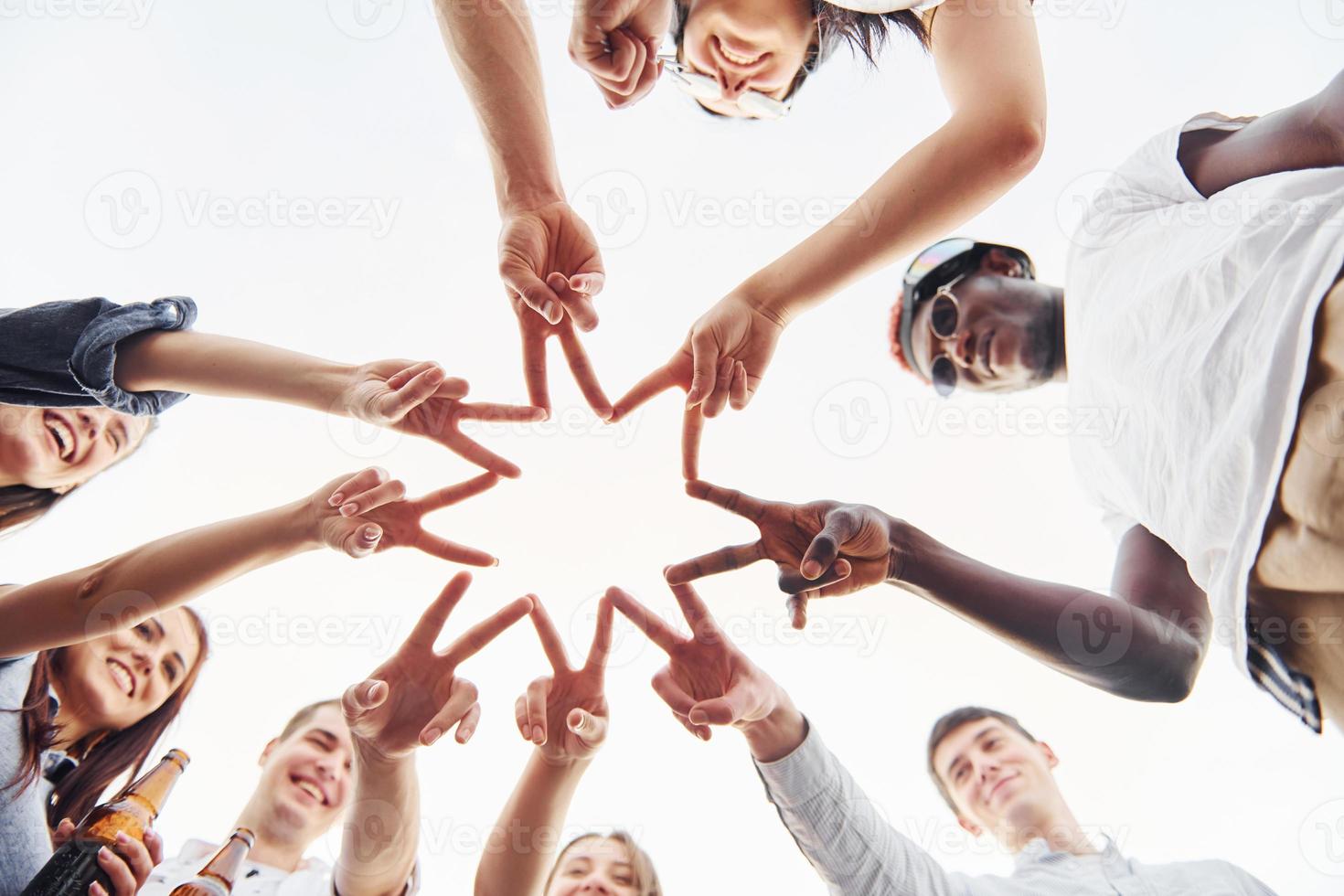 Making beautiful gesture by fingers. View from below. Group of young people in casual clothes have a party at rooftop together at daytime photo