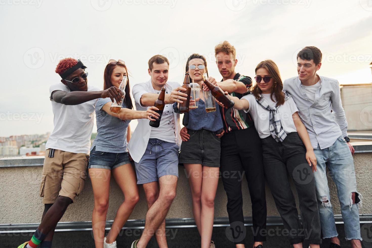 de pie con alcohol en el borde de la azotea. grupo de jóvenes con ropa informal tienen una fiesta juntos durante el día foto
