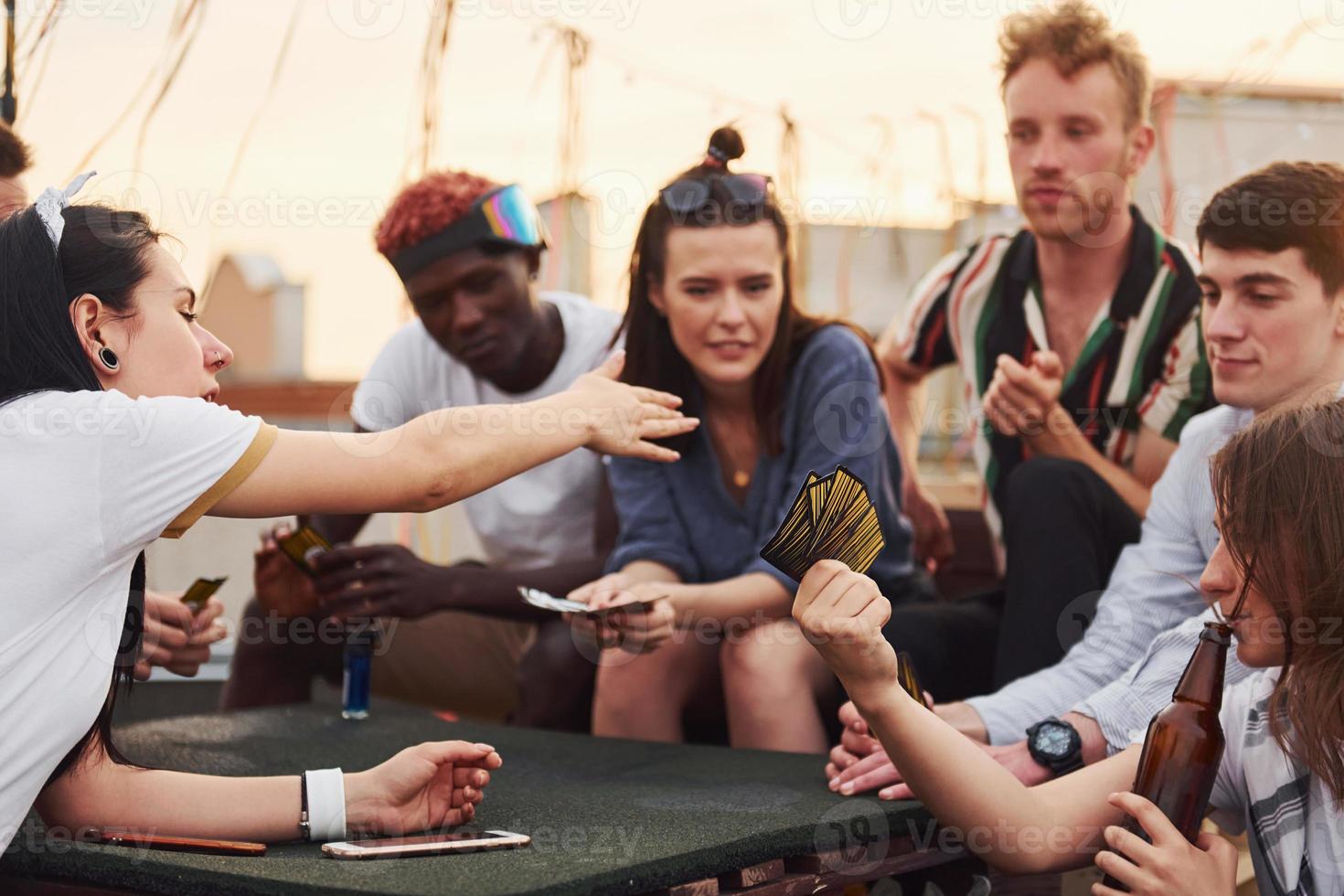 Sitting by table and playing card game. Group of young people in casual