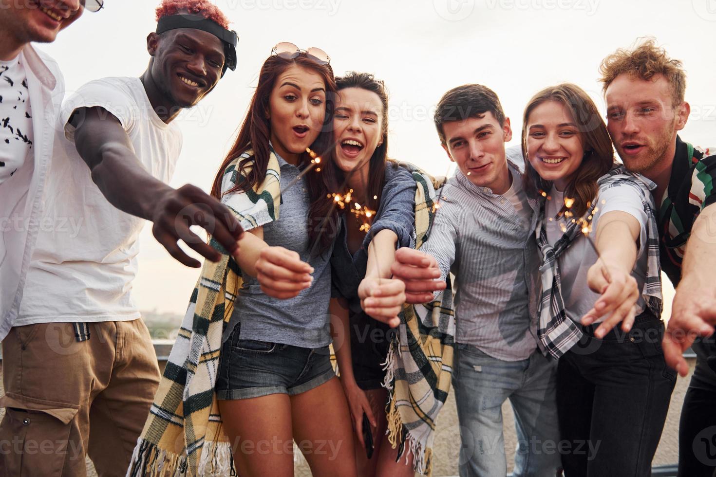 con bengalas en las manos. un grupo de jóvenes con ropa informal tienen una fiesta en la azotea juntos durante el día foto