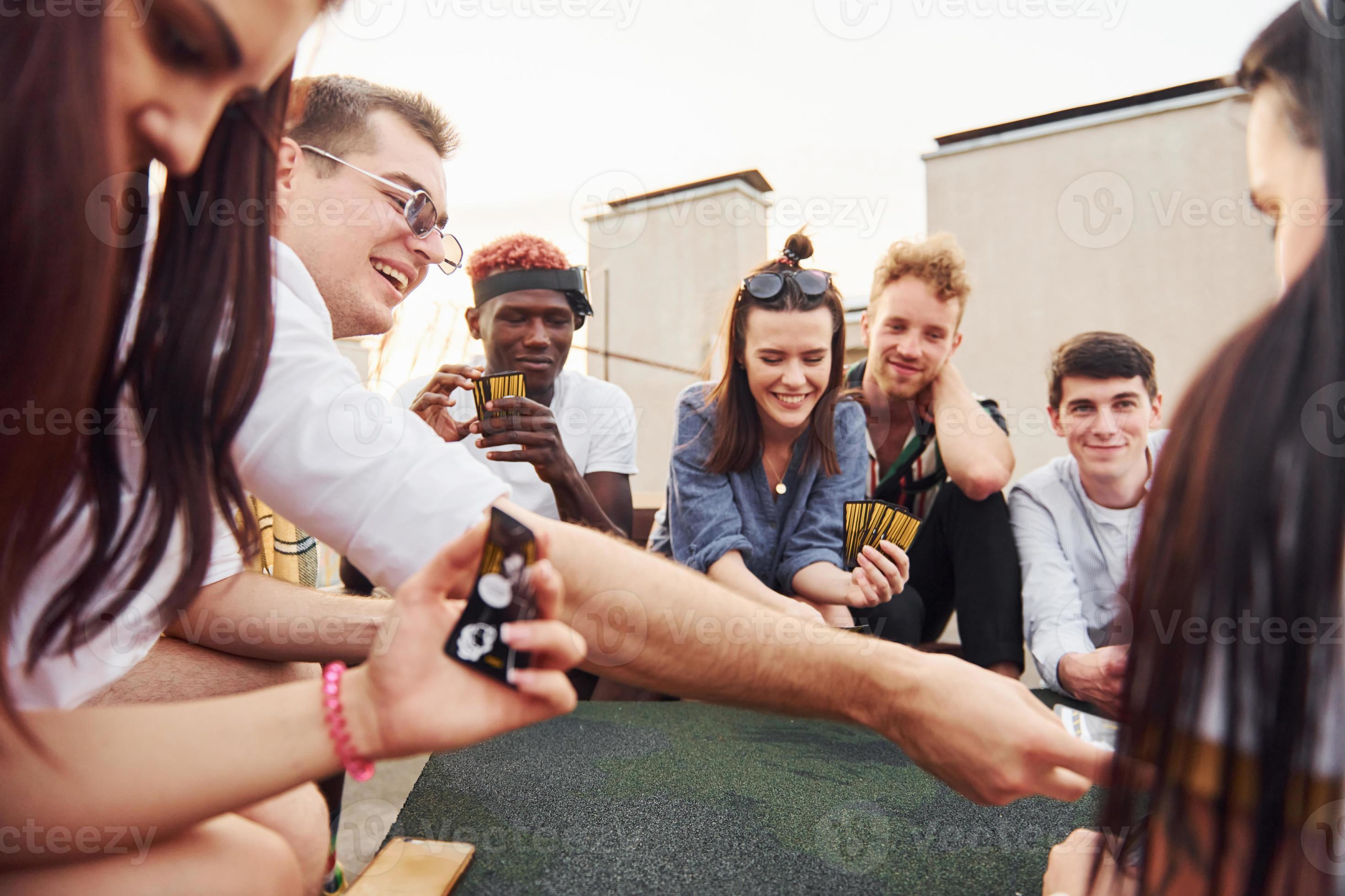 Sitting by table and playing card game. Group of young people in casual