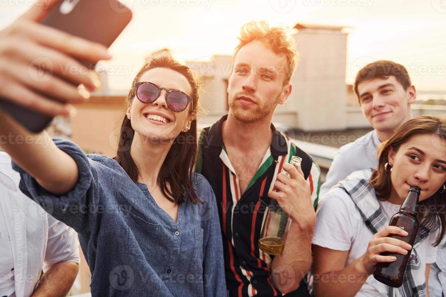 Taking selfie. Beautiful sunshine. Group of young people in casual clothes have a party at rooftop together at daytime photo