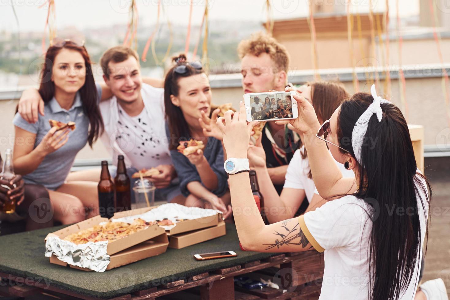 haciendo foto. deliciosa pizza un grupo de jóvenes con ropa informal tienen una fiesta en la azotea juntos durante el día foto