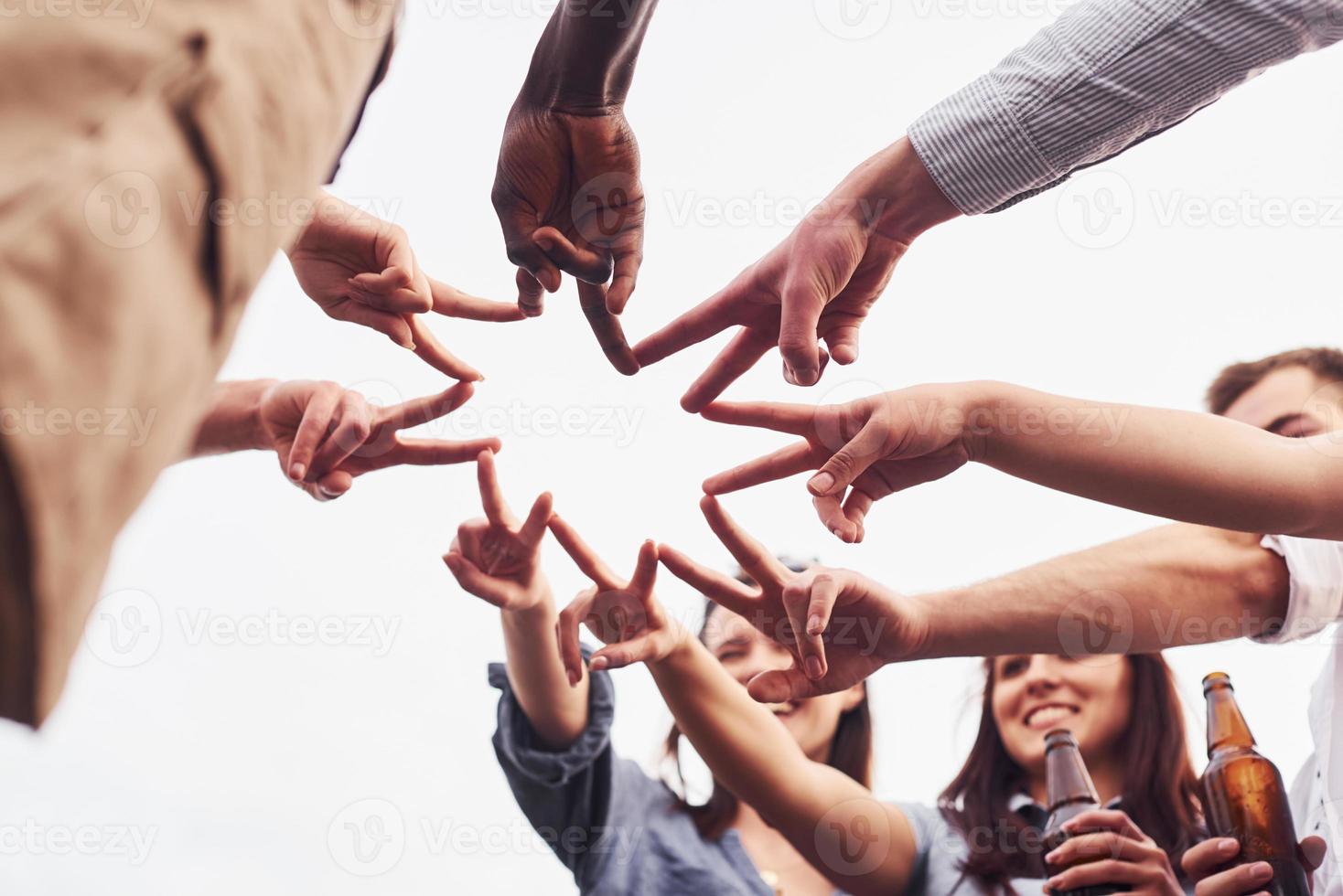 Making beautiful gesture by fingers. View from below. Group of young people in casual clothes have a party at rooftop together at daytime photo