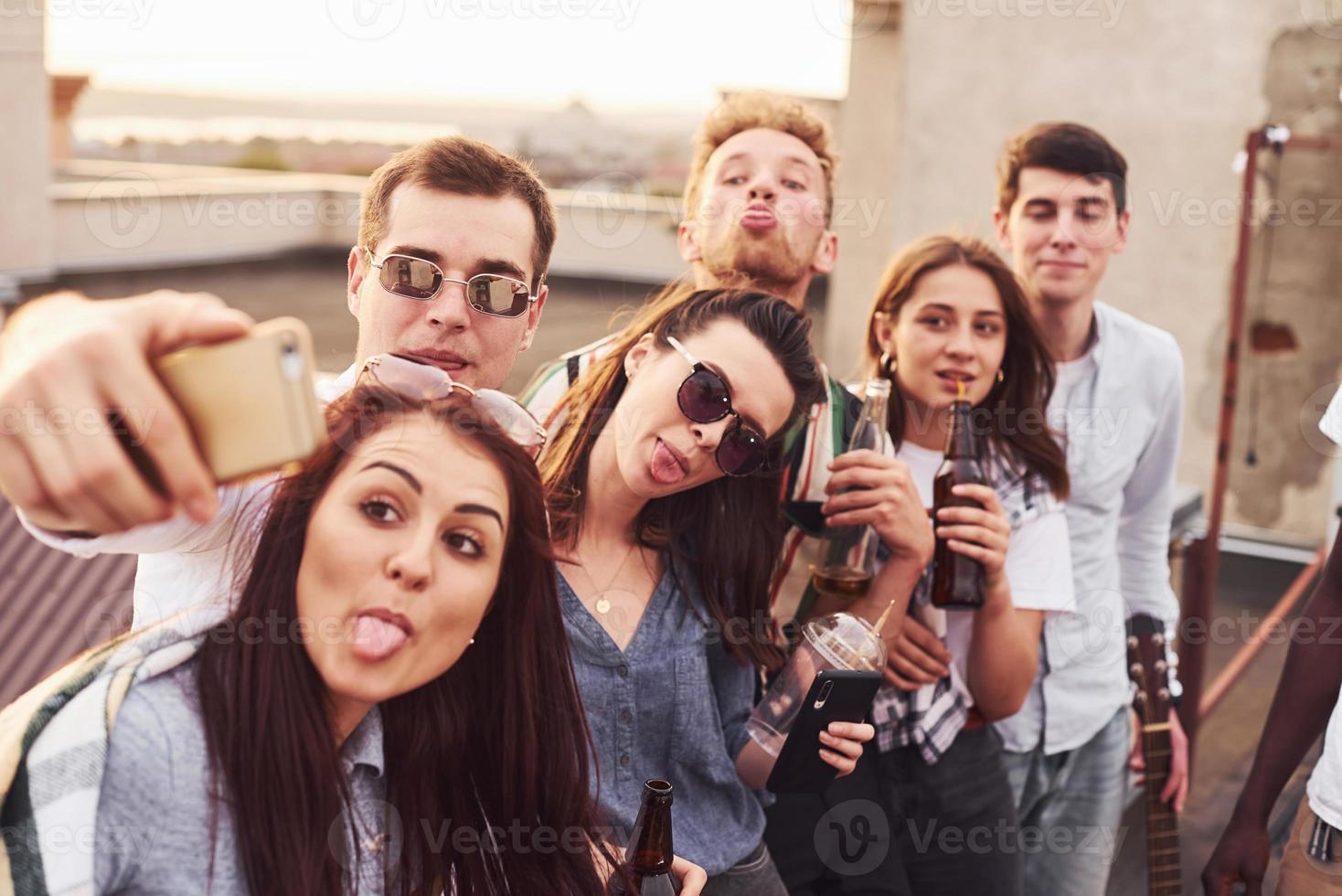 haciendo selfie por teléfono. un grupo de jóvenes con ropa informal tienen una fiesta en la azotea juntos durante el día foto