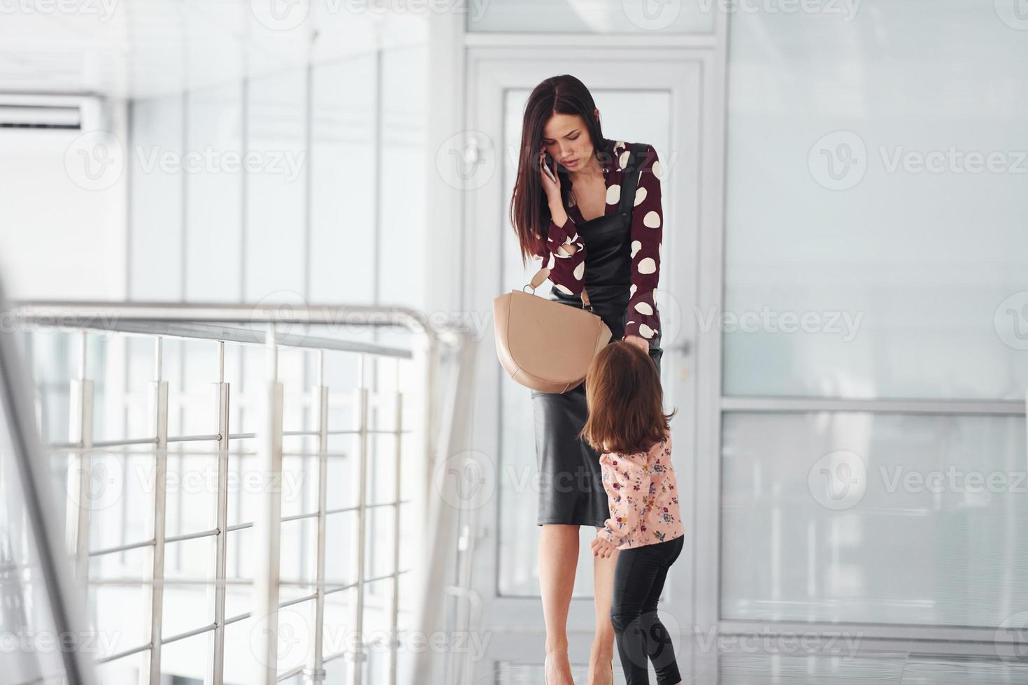 Young mother with her daughter walking together indoors in the office or airport. Having vacation photo