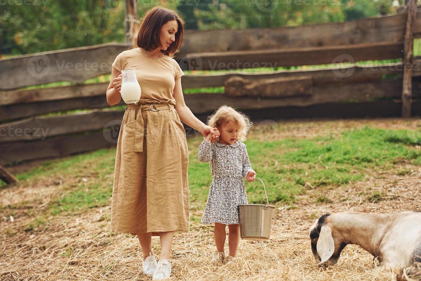 Fresh natural milk. Young mother with her daughter is on the farm at summertime with goats photo