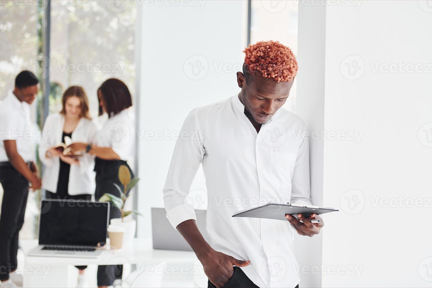 Man with notepad standing in front of colleagues. Group of african american business people working in office together photo