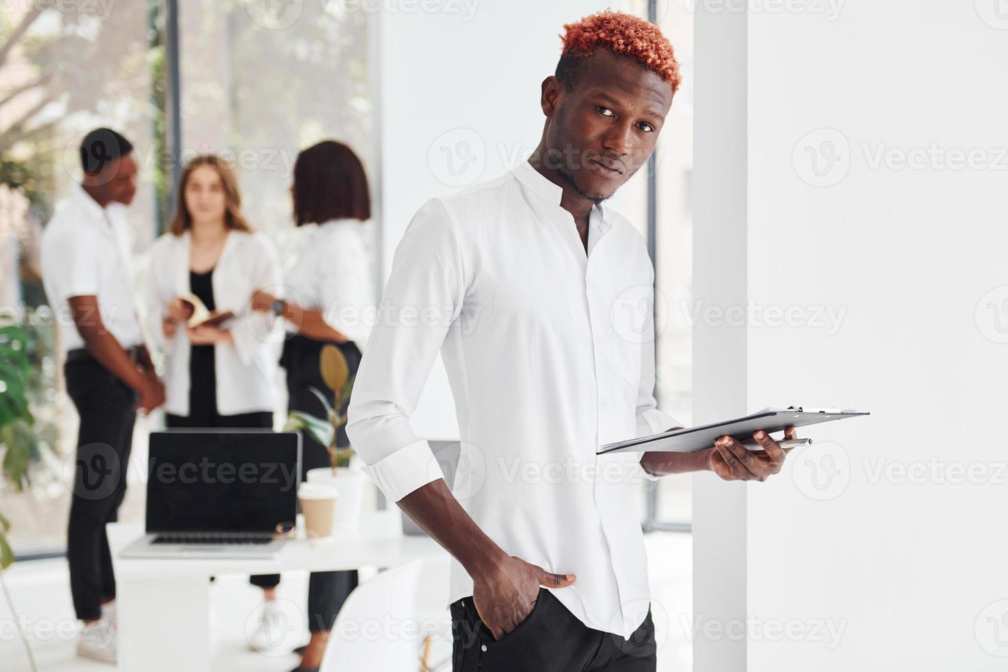 Man with notepad standing in front of colleagues. Group of african american business people working in office together photo