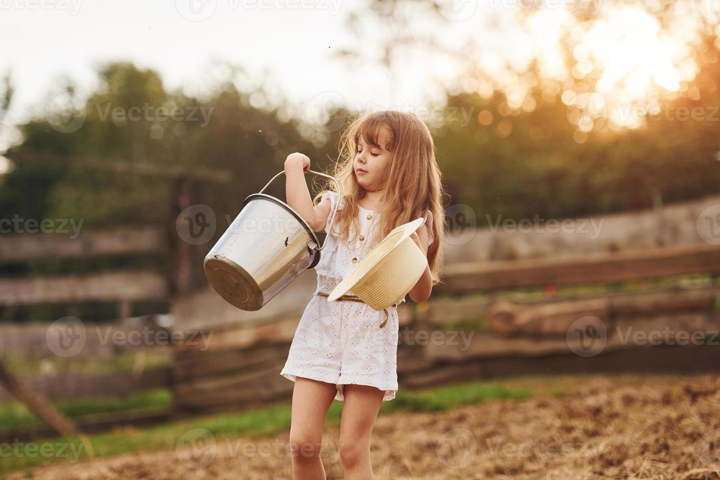 Little girl in white clothes is on the farm at summertime outdoors with milk photo