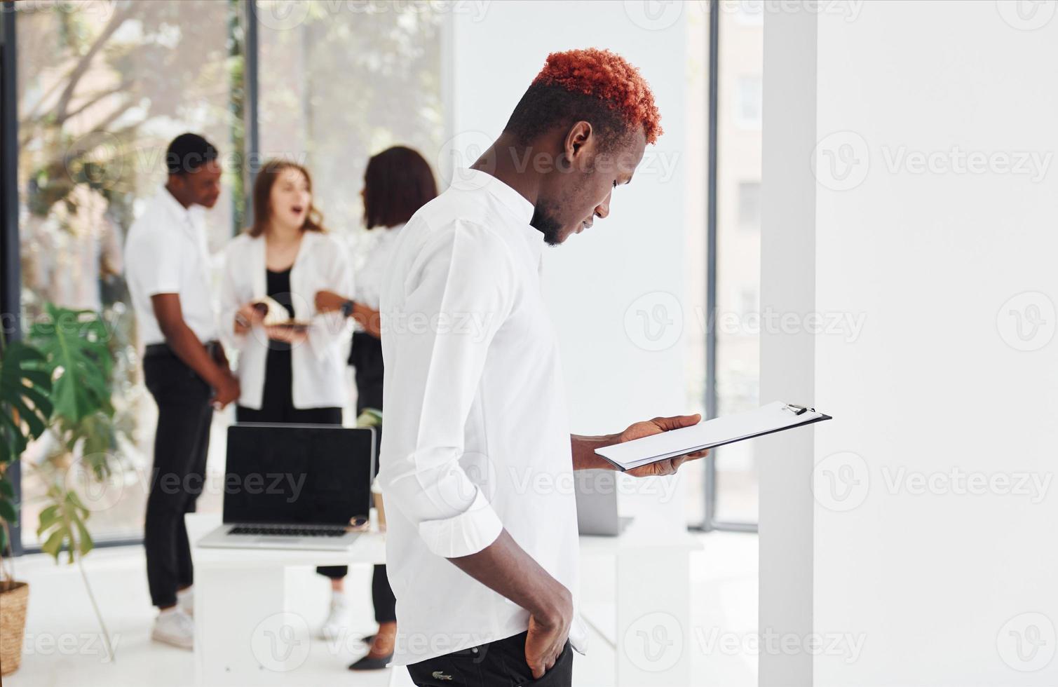 Man with notepad standing in front of colleagues. Group of african american business people working in office together photo
