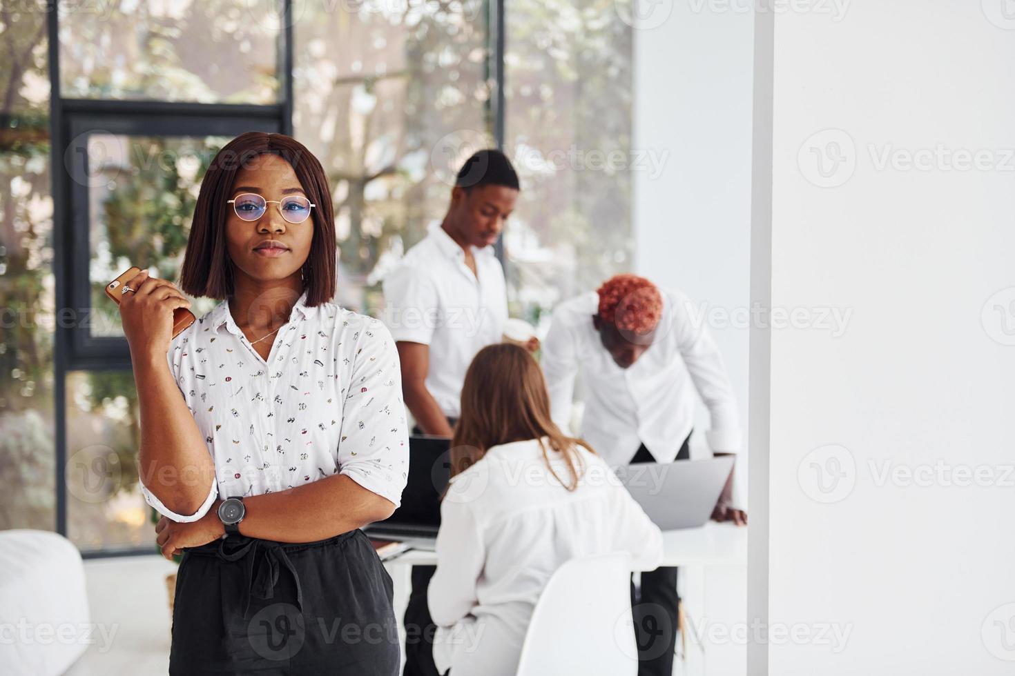 Beautiful woman in glasses in front of her colleagues. Group of african american business people working in office together photo