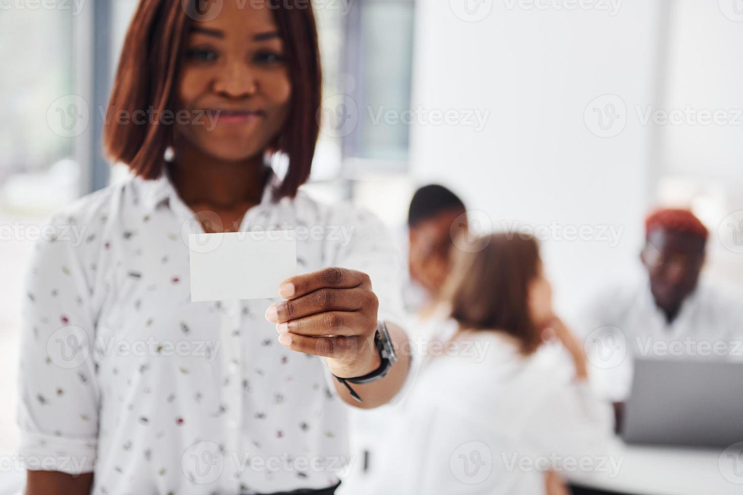Woman holds business card card. Group of african american people working in office together photo
