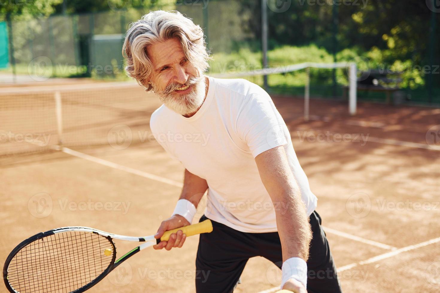 Playing game. Senior modern stylish man with racket outdoors on tennis court at daytime photo