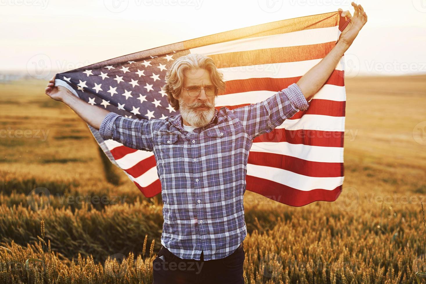 Patriotic senior man standing on the field with USA flag. Conception of freedom photo