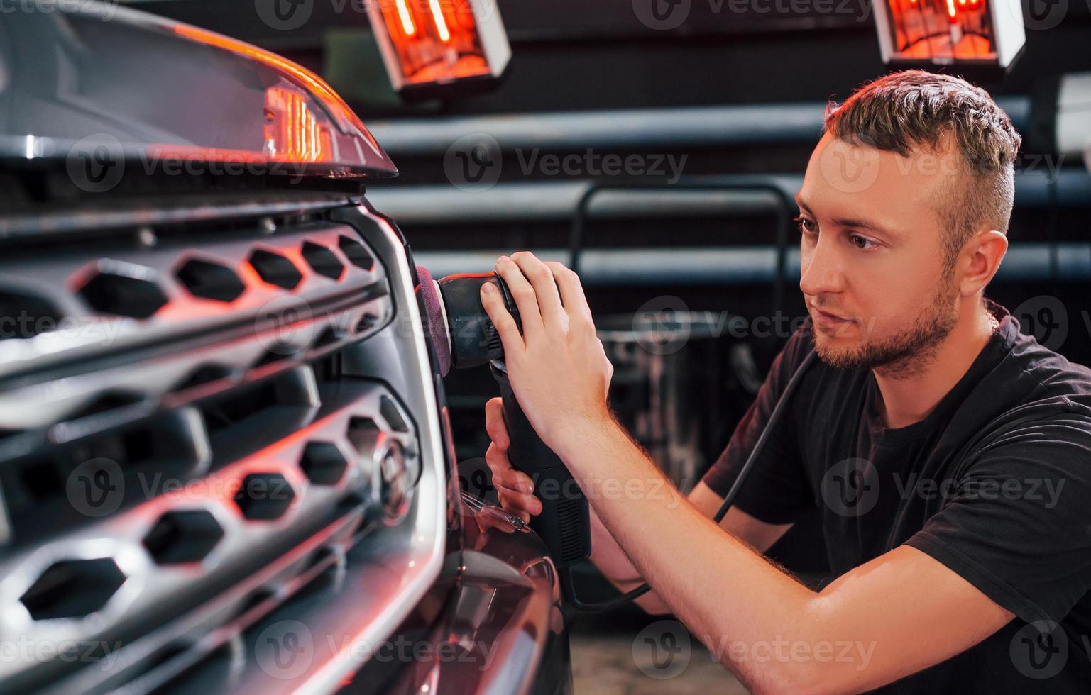 Guy polishing surface of vehicle. Modern black automobile get cleaned by man inside of car wash station photo