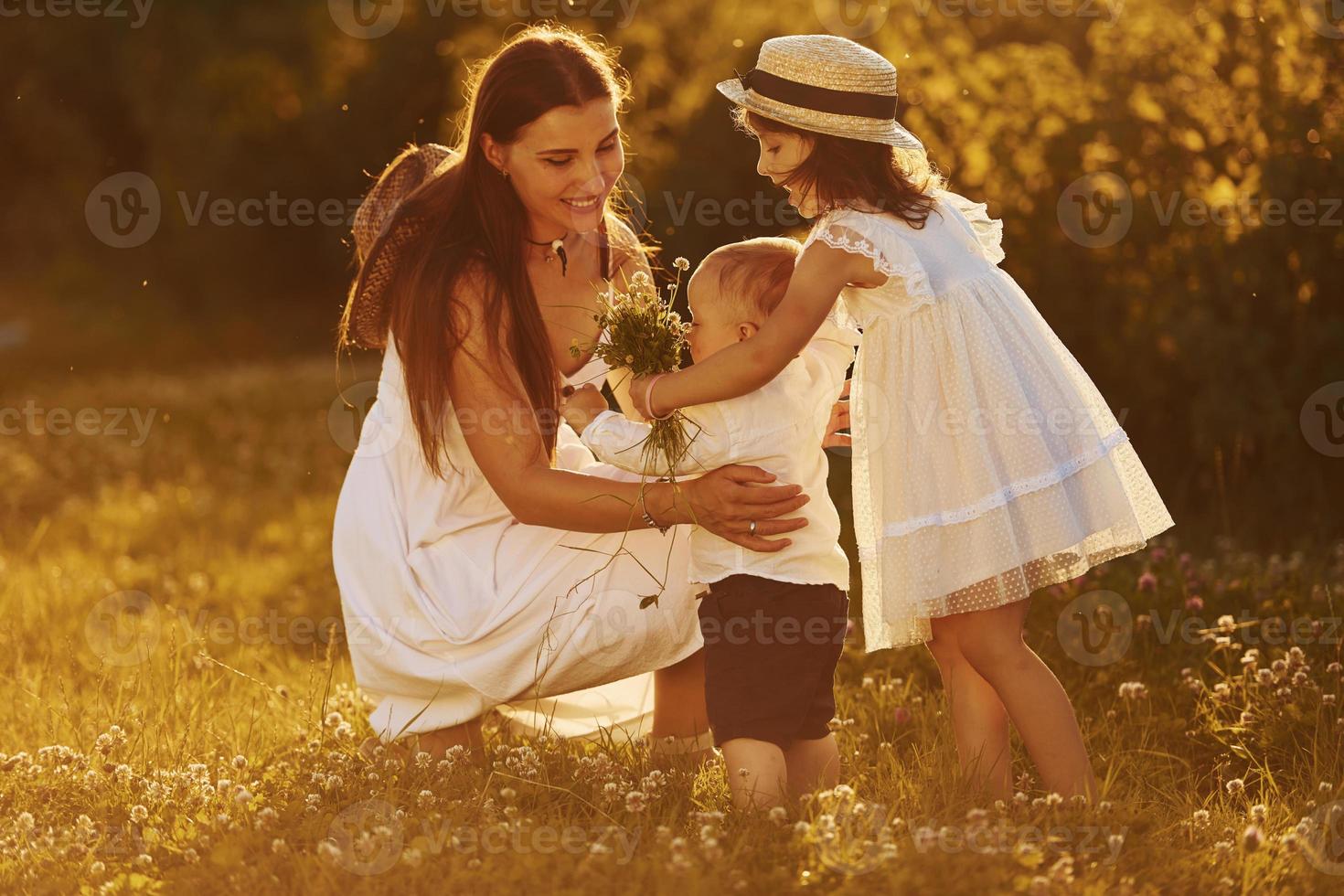Happy family of mother, little son and daughter spending free time on the meadow at sunny day time of summer photo