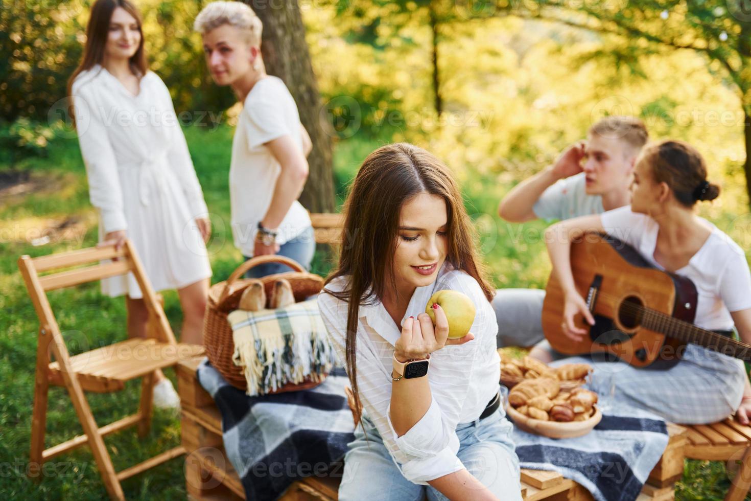Woman eats apple. Group of young people have vacation outdoors in the forest. Conception of weekend and friendship photo