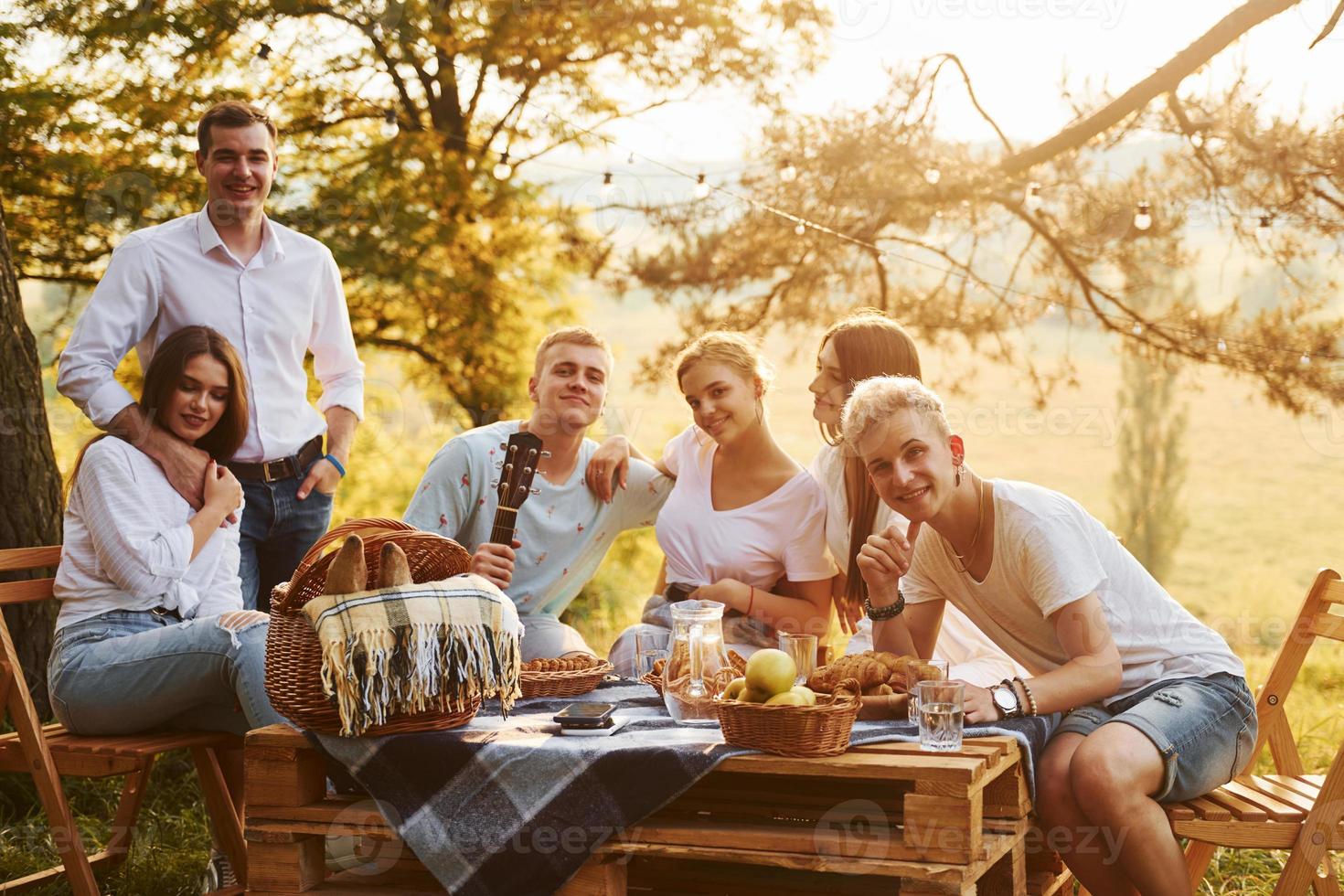 Sitting by picnic table. Group of young people have vacation outdoors