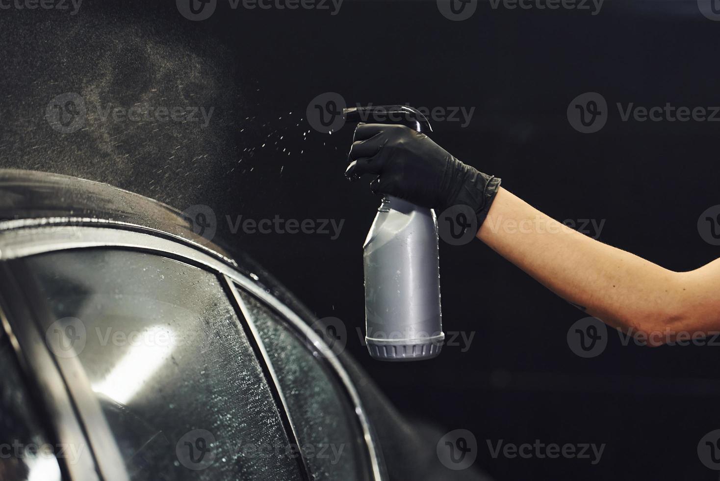 Spraying the vehicle. Modern black automobile get cleaned by woman inside of car wash station photo