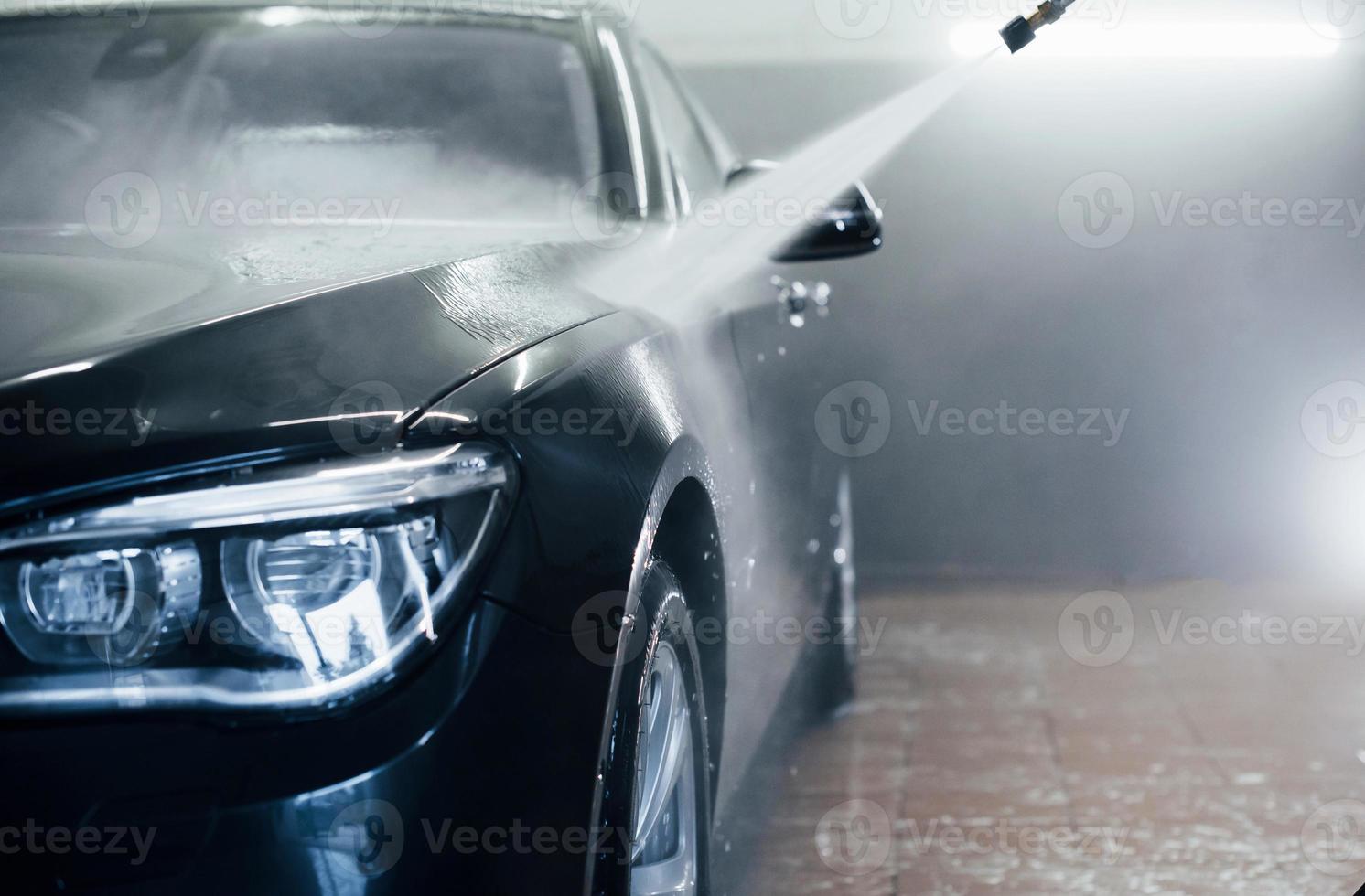 agua a alta presión. automóvil negro moderno se limpia dentro de la estación de lavado de autos foto