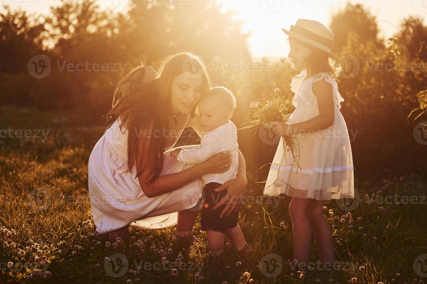 Cheerful family of mother, little son and daughter spending free time on the field at sunny day time of summer photo