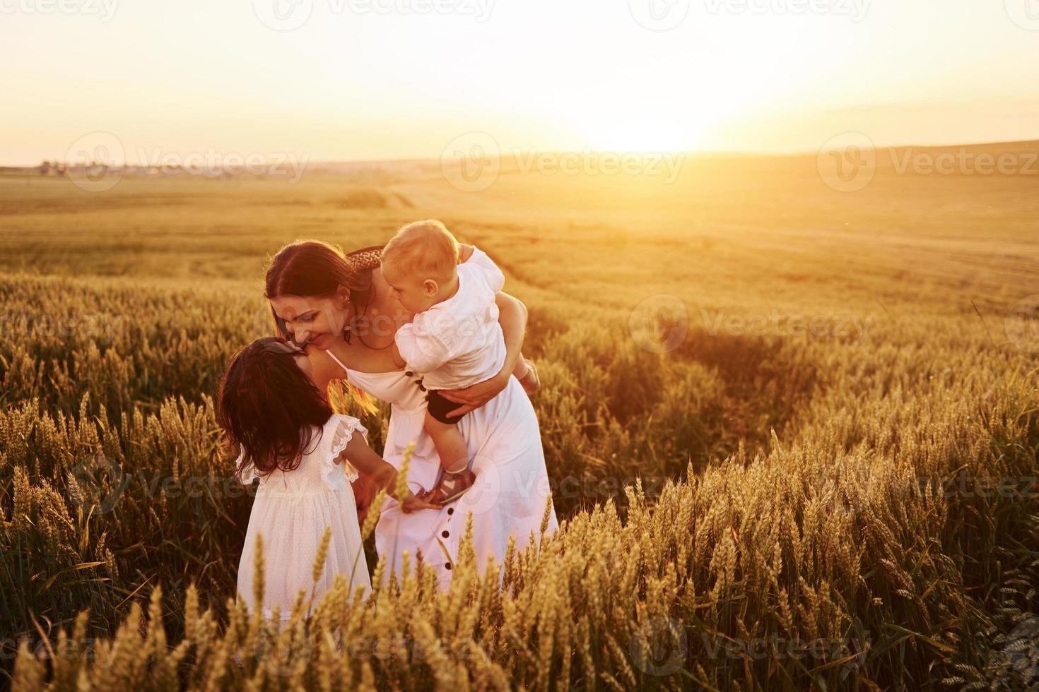 Cheerful family of mother, little son and daughter spending free time on the field at sunny day time of summer photo