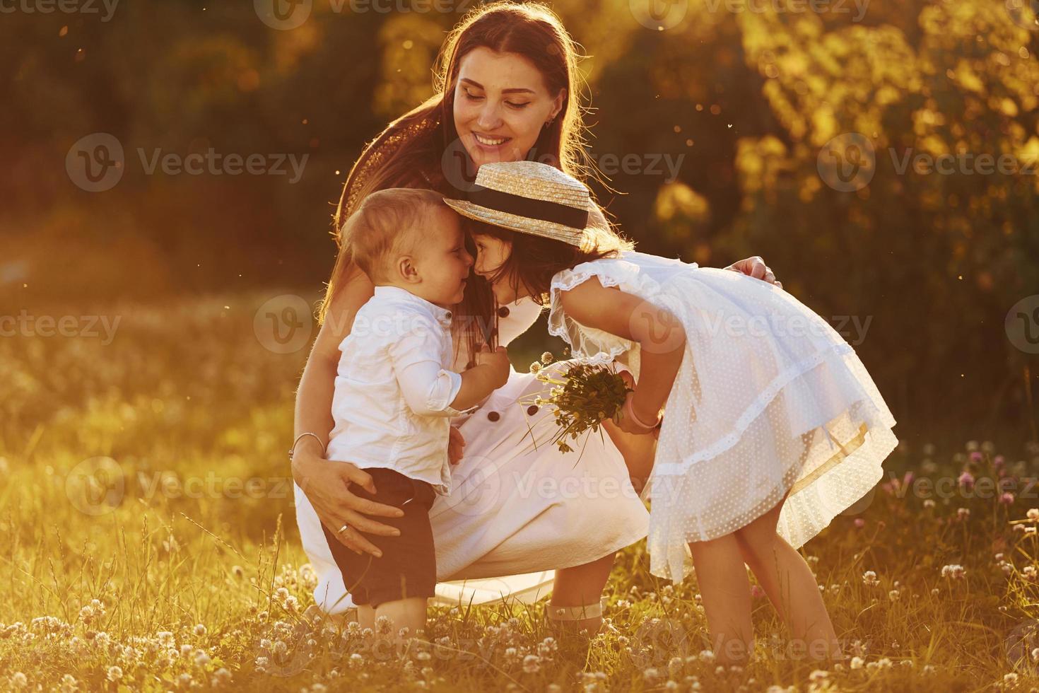 Happy family of mother, little son and daughter spending free time on the meadow at sunny day time of summer photo