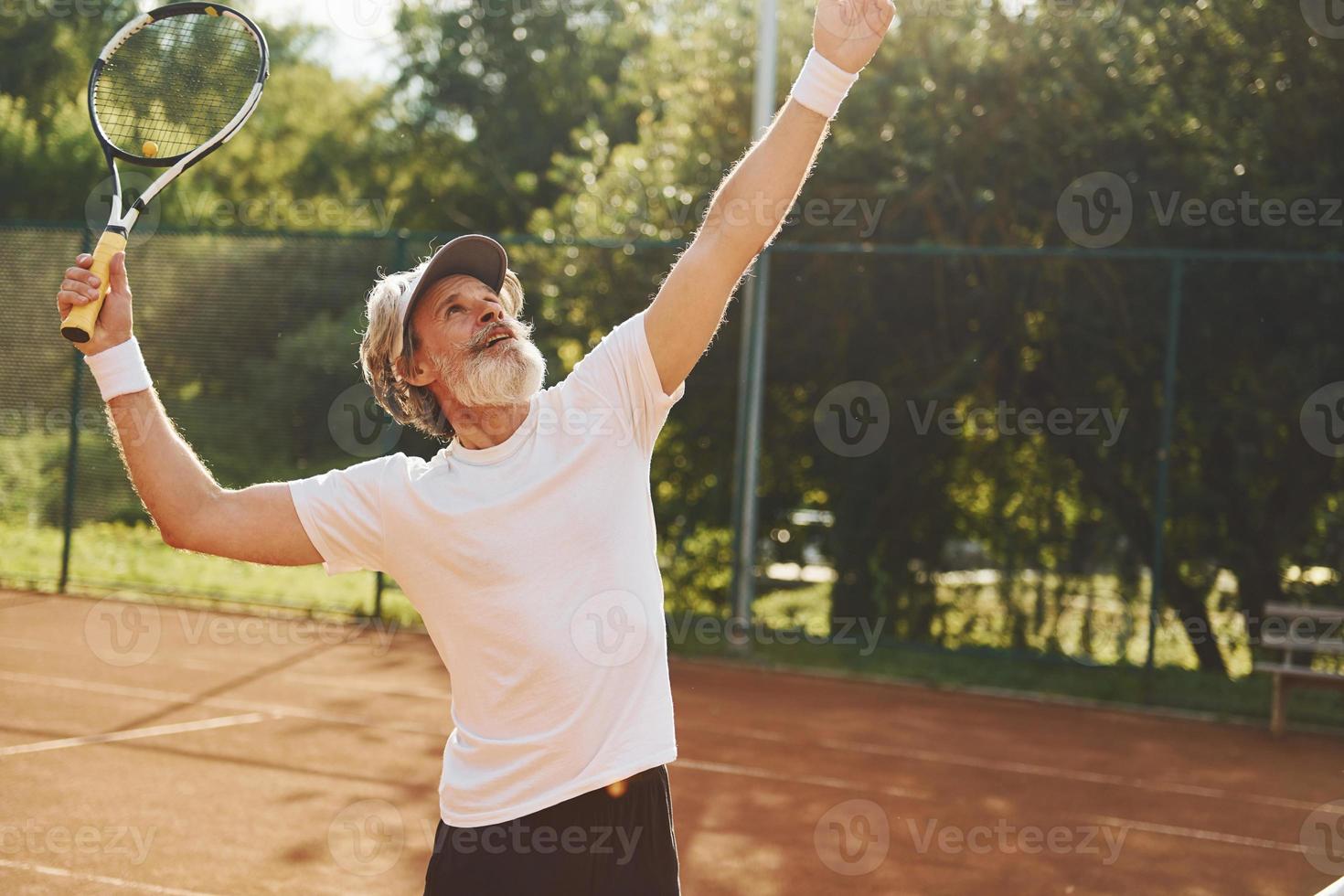 jugando un juego. Senior hombre moderno y elegante con raqueta al aire libre en la cancha de tenis durante el día foto