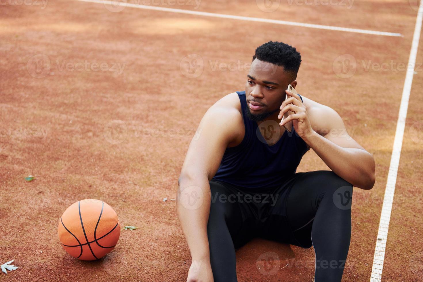 habla por teléfono. hombre afroamericano juega baloncesto en la cancha al aire libre foto