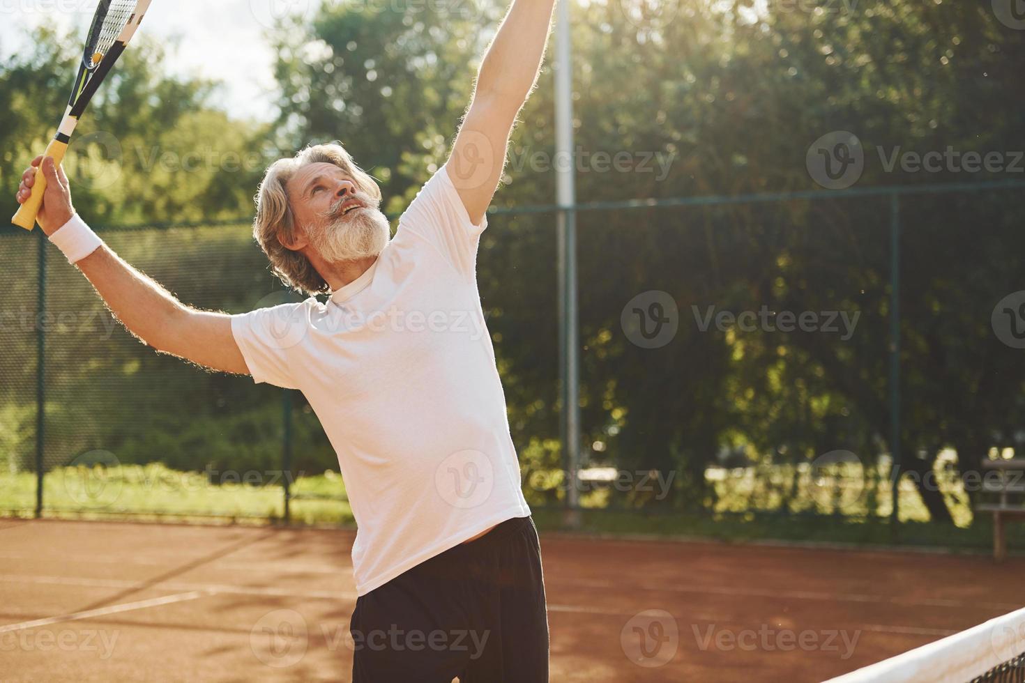 jugando un juego. Senior hombre moderno y elegante con raqueta al aire libre en la cancha de tenis durante el día foto